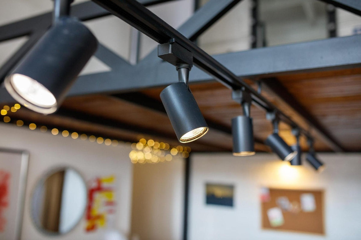 Black modern track lighting heads mounted under an exposed ceiling beam